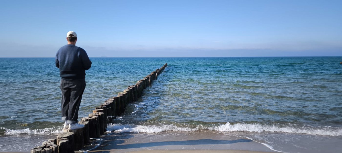 Ein Mann steht am Ende eines Stegs und schaut auf das Meer