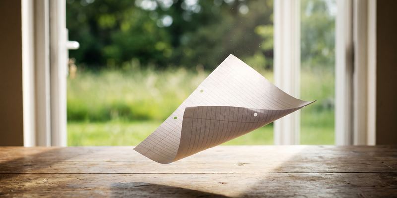 Ein leeres Blatt Papier wird vom Wind durch die offene Gartentür vom Tisch gehoben